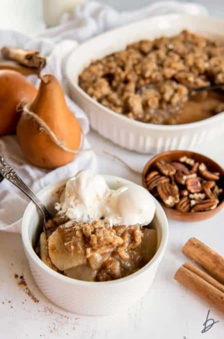 A bowl of the Best Pear Crisp with Oats on a white counter top with the rest of the crisp in the background.
