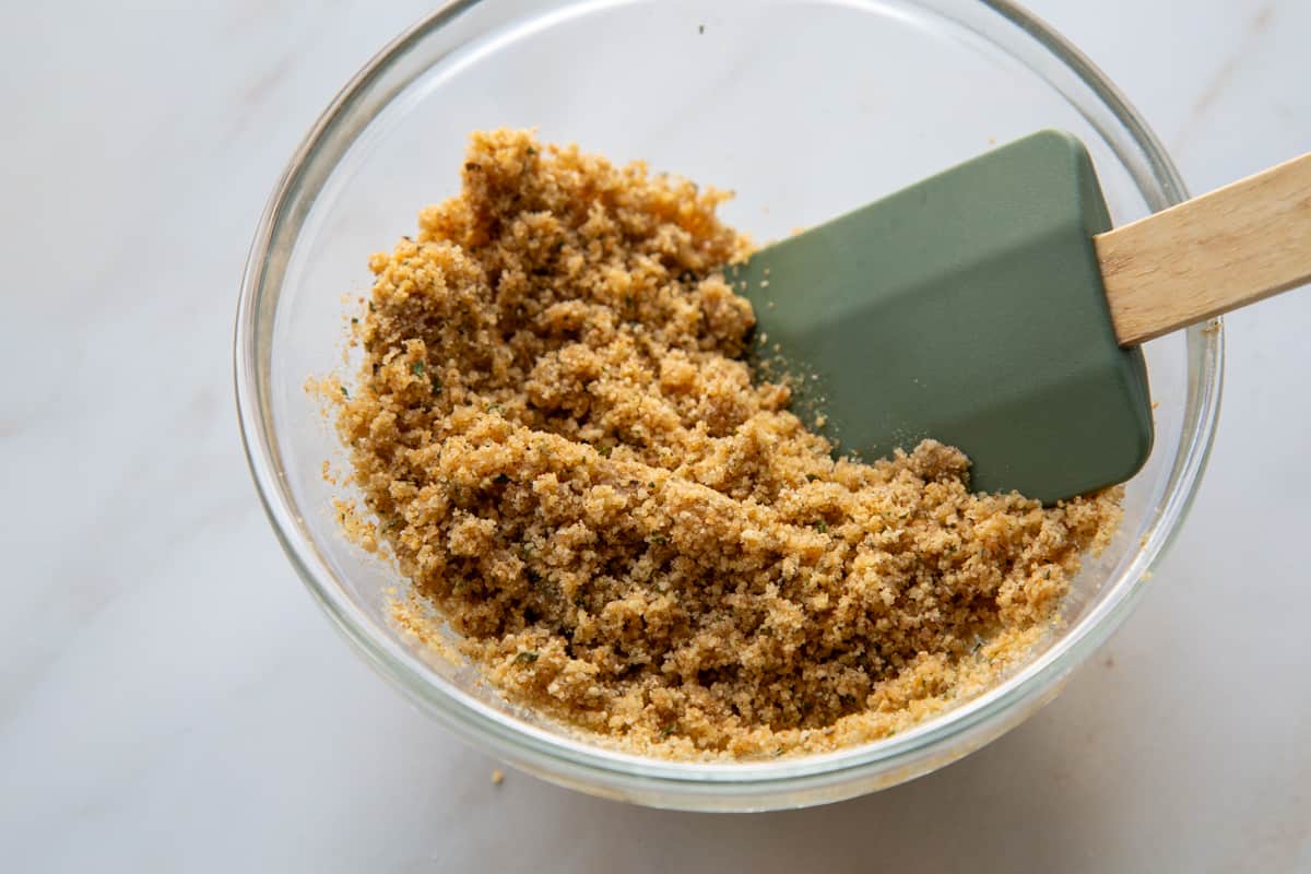 breadcrumb mixture in a glass bowl with a spatula.