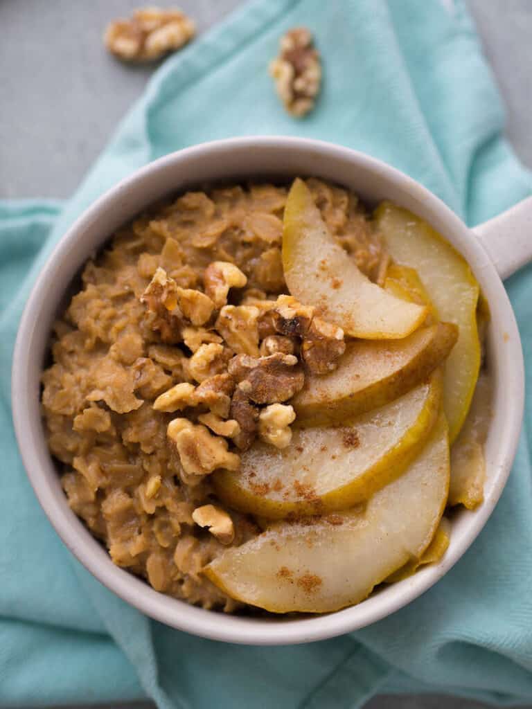 Top view of a bowl of Chai Oatmeal with Spiced Sauteed Pears on a light aqua colored napkin.