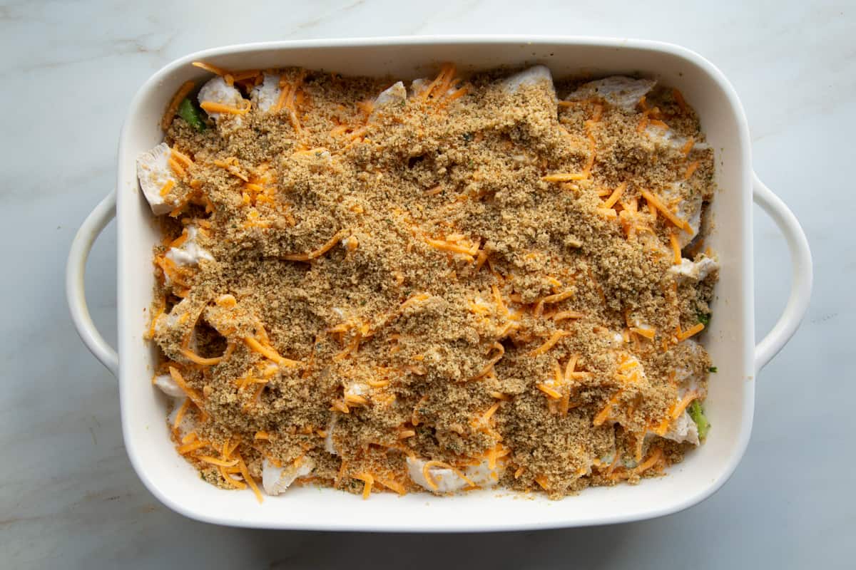 breadcrumbs and cheddar on top of chicken in a casserole dish. 