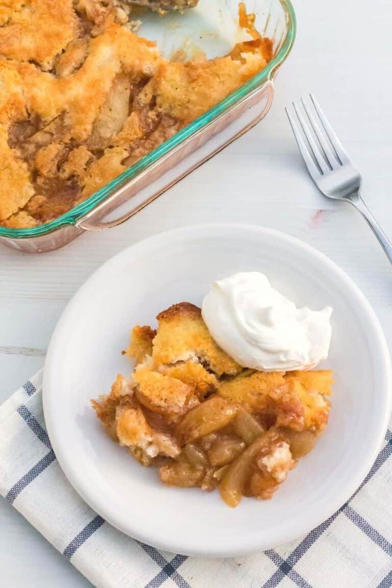 Top view of a serving of Pear Cobbler on a small white plate with a dollop of whipped cream.