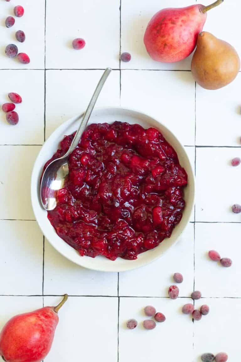 Overhead view of a small white bowl of Cranberry Pear Sauce on a white tiled surface.