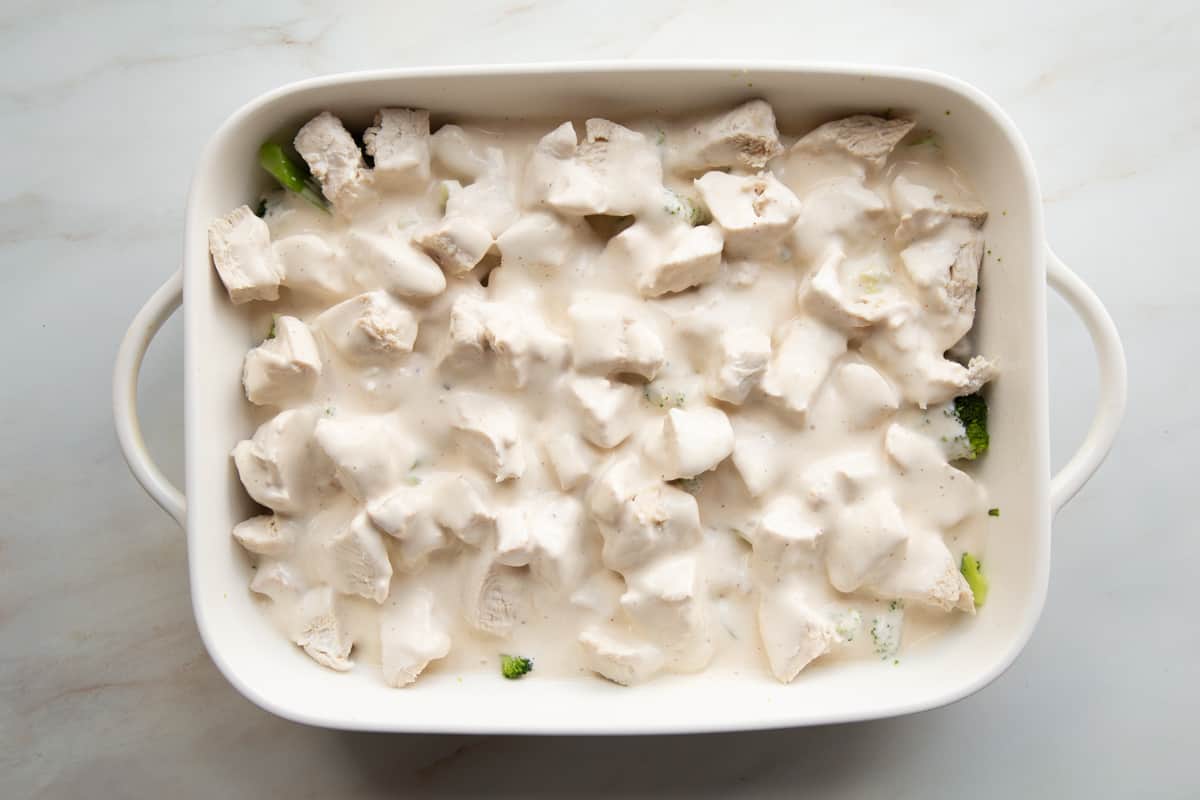 chicken and broccoli topped with a white creamy sauce in a baking pan.