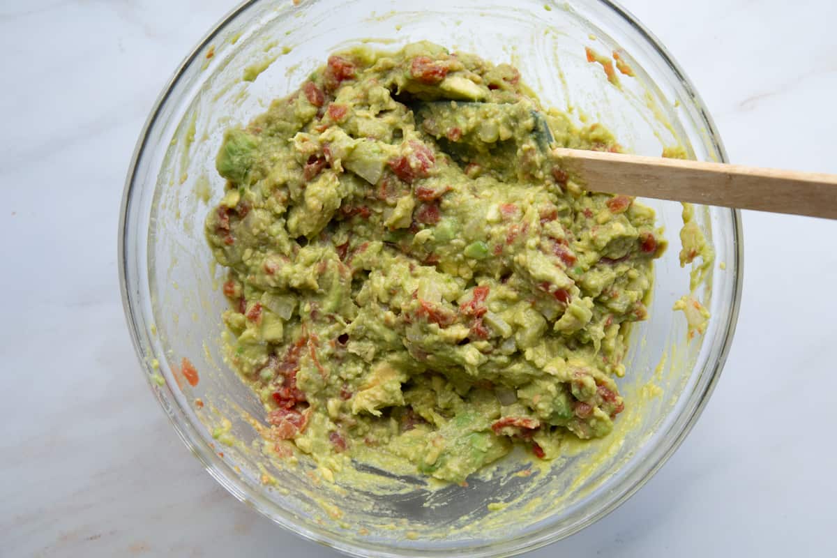 Glass mixing bowl of Rotel Guacamole with a spatula in it.
