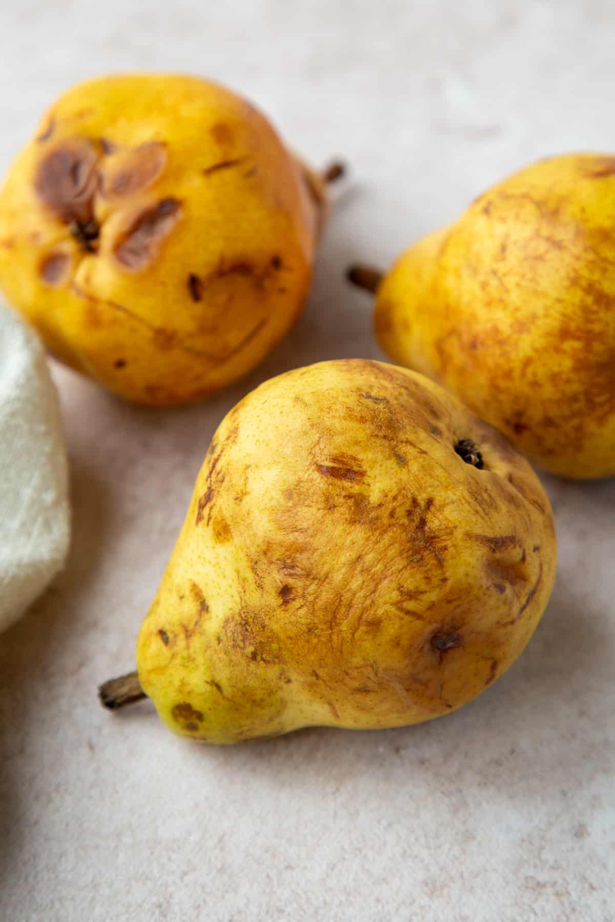 Close up of 3 overripe pears on a gray surface.