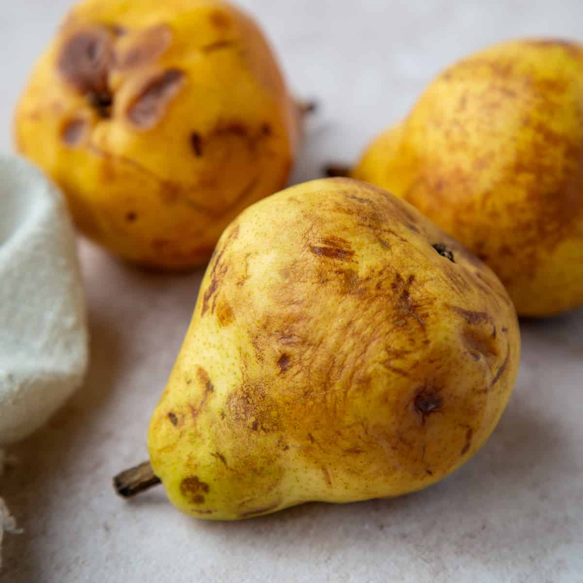 Close up of 3 overripe pears on a gray surface.