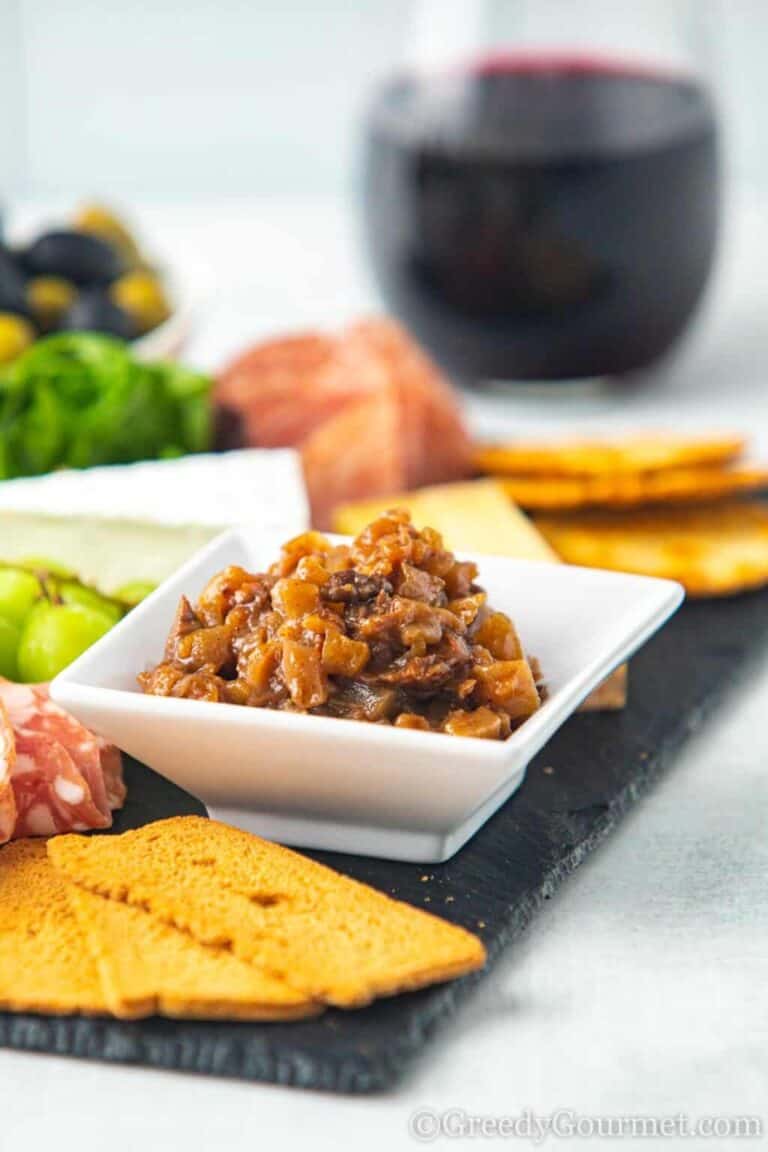 A small white bowl of Pear Chutney on a cutting board with meat, fruit and crackers.