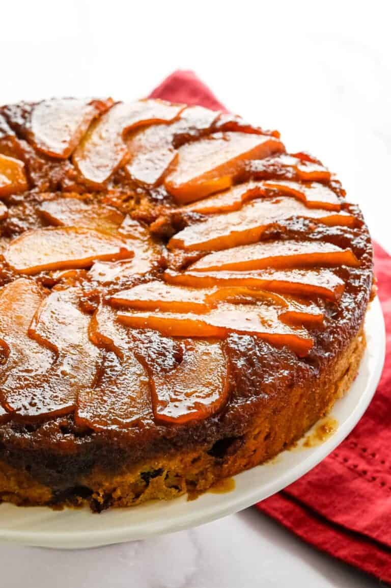 Side view of a Pear Cranberry Upside Down Cake on a white cake plate with a red napkin below.