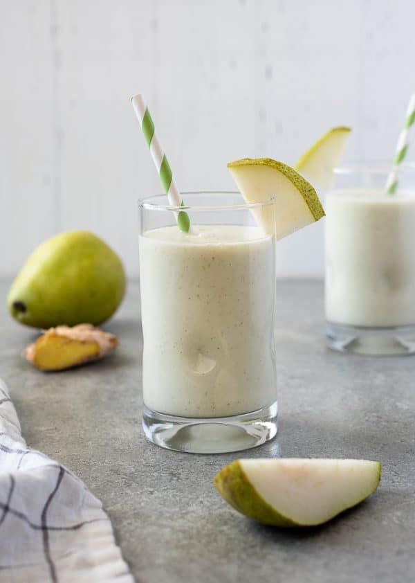 Side view of a Pear Ginger Smoothie with a striped green straw in a glass cup.