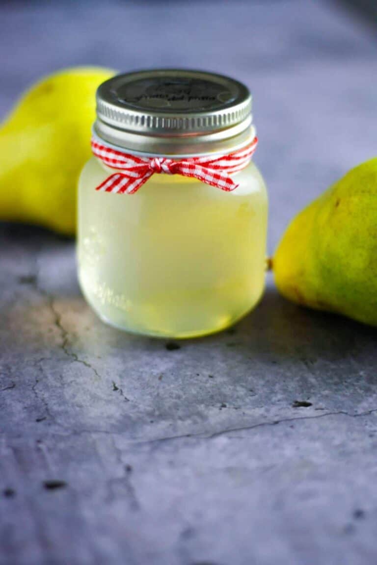 A small jar of Pear Simple Syrup tied with a red and white checkered ribbon on a blue marble surface.