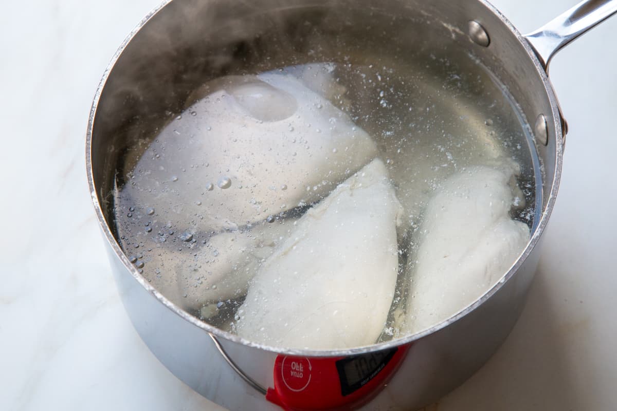 Chicken in a saucepan being poached.