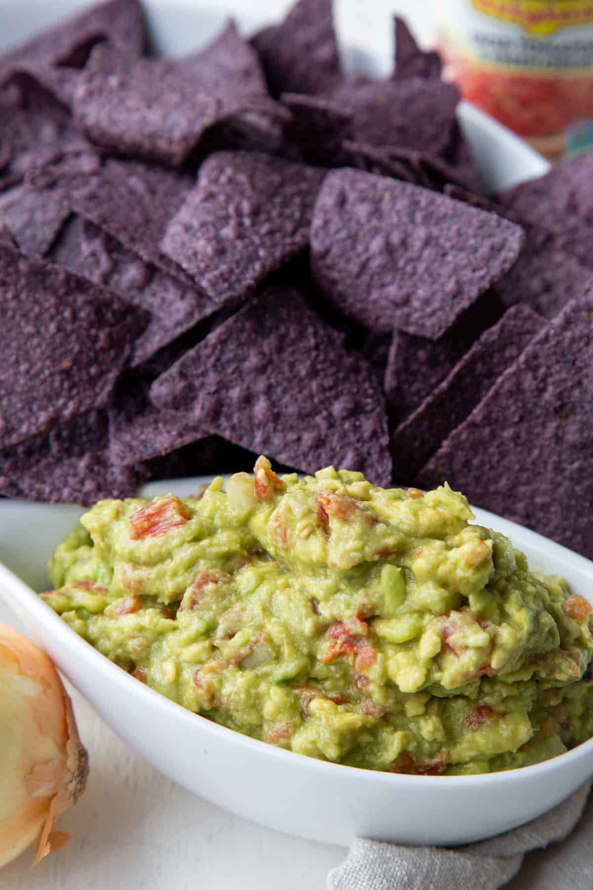 A white container of Rotel Guacamole next to an onion and blue corn tortilla chips.