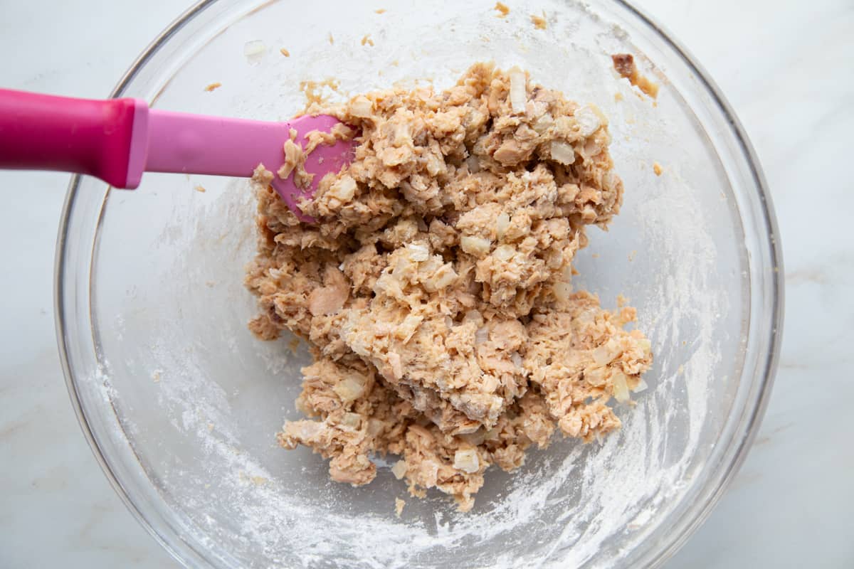 Salmon Patty mixture in a clear glass mixing bowl with a pink mixing spoon.