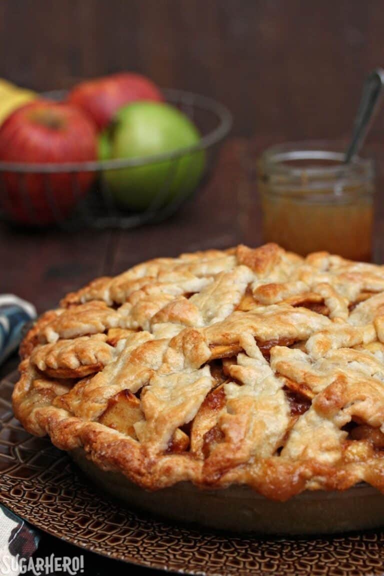 Side view of a Pear Apple Pie with Salted Caramel Sauce on a brown textured plate with apples in the background