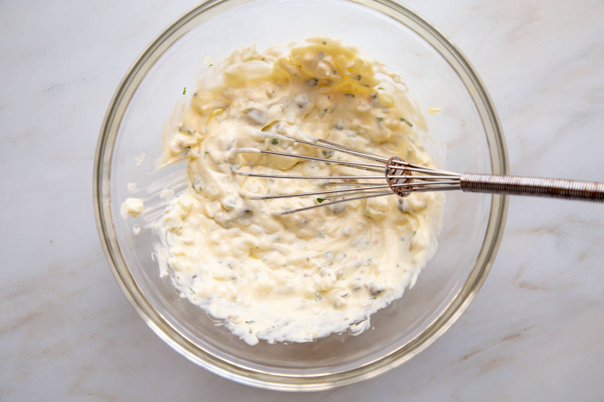 Top view of a whisk in a clear mixing bowl of Tartar Sauce.