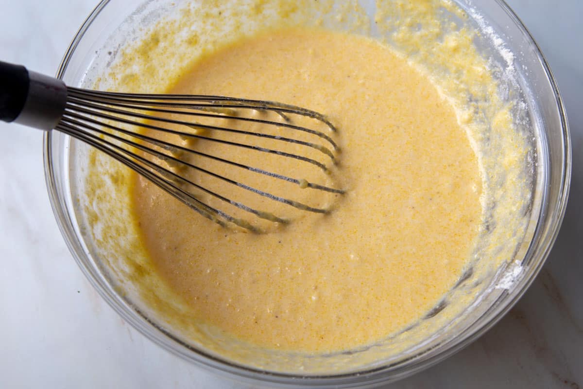 cornbread batter in a glass mixing bowl with a whisk.