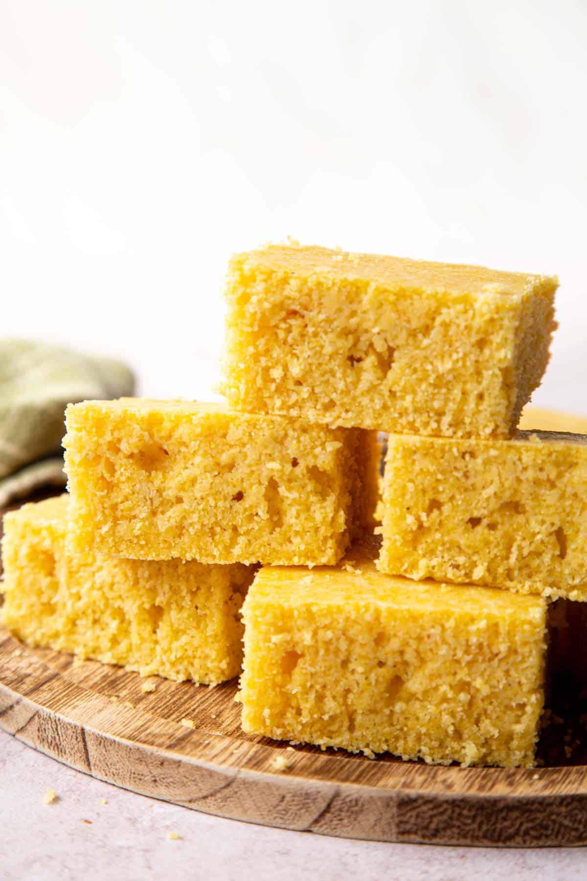 5 old fashioned cornbread slices stacked on a wooden surface.