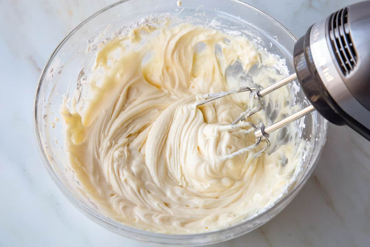 cream cheese frosting in a glass mixing bowl with a handheld mixer.