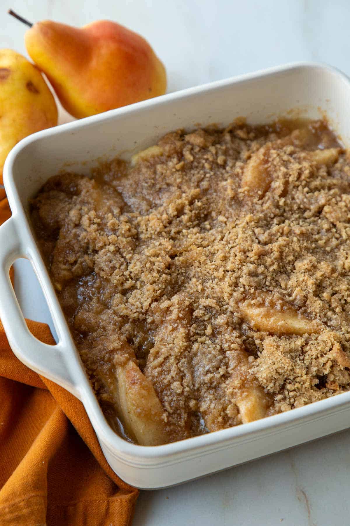 old fashioned pear crumble in a white baking dish next to fresh pears.