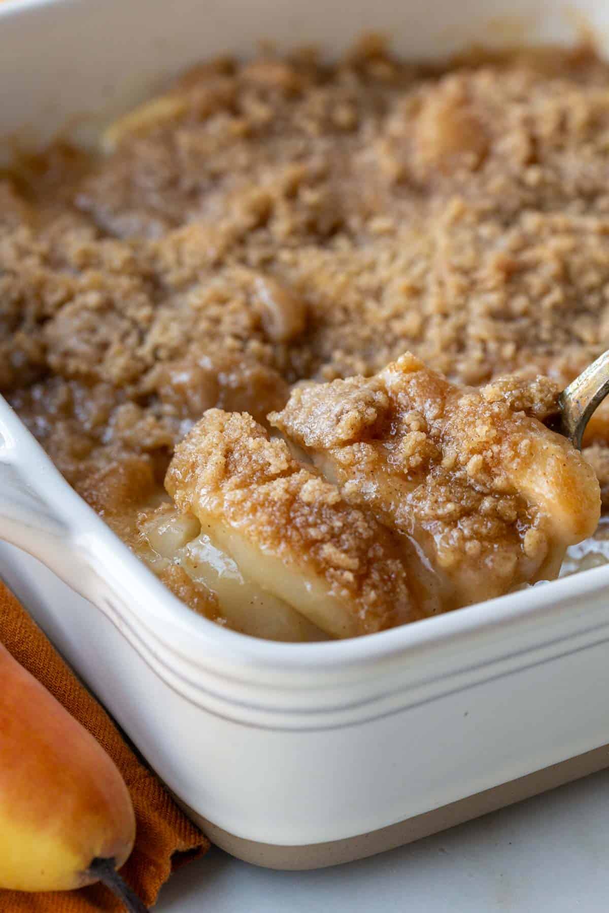 A spoon lifting a serving of Pear Crumble from the baking dish.