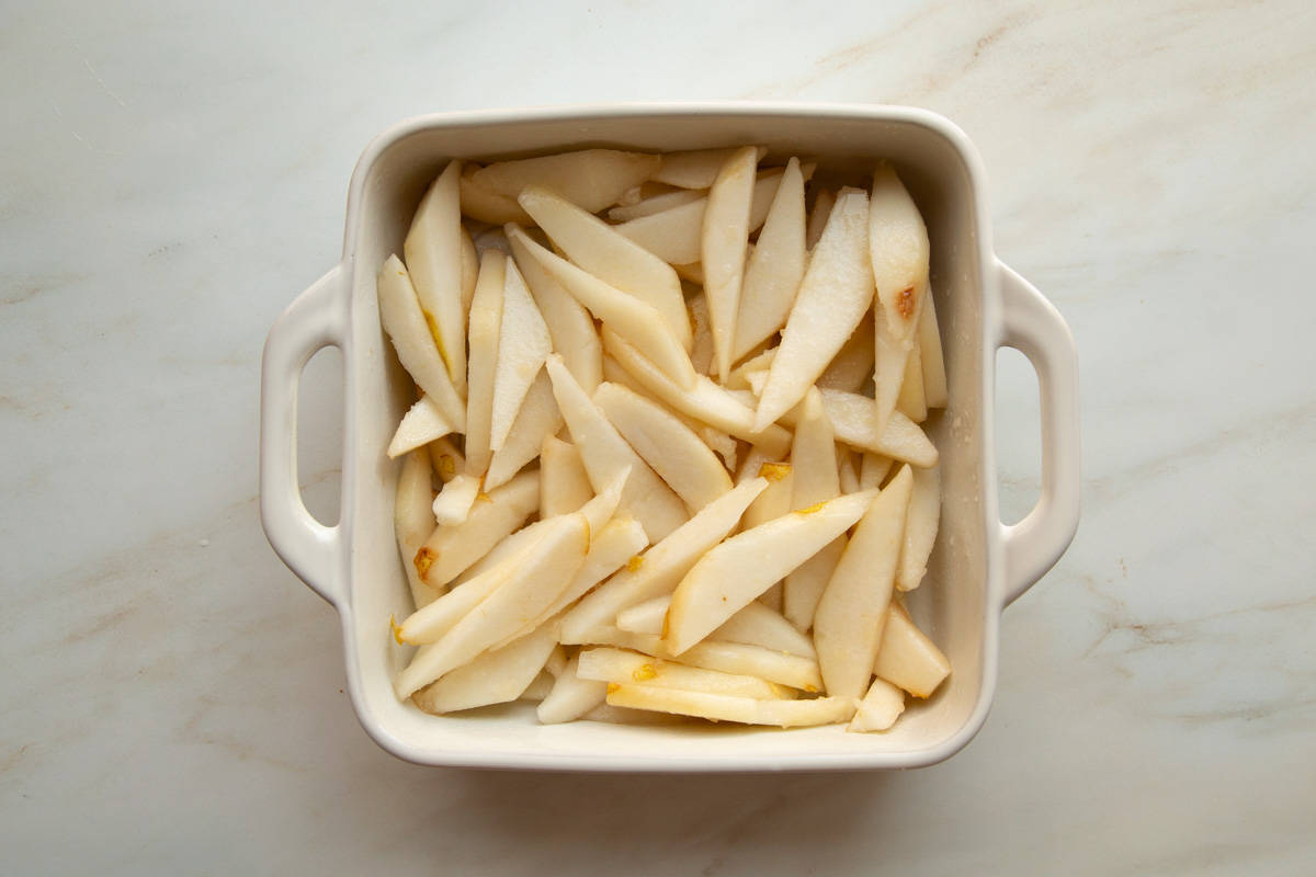 Sliced pears covered in lemon juice in a white ceramic baking dish.