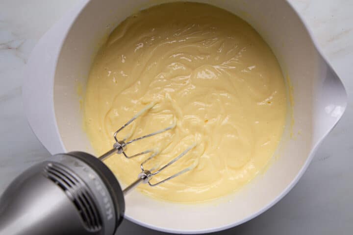 vanilla pudding being mixed in a white mixing bowl with a hand mixer.