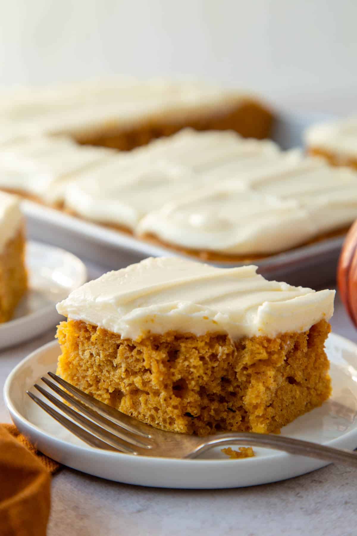 A slice of Pumpkin Bar with Cream Cheese Frosting with a bite removed on a small white plate.