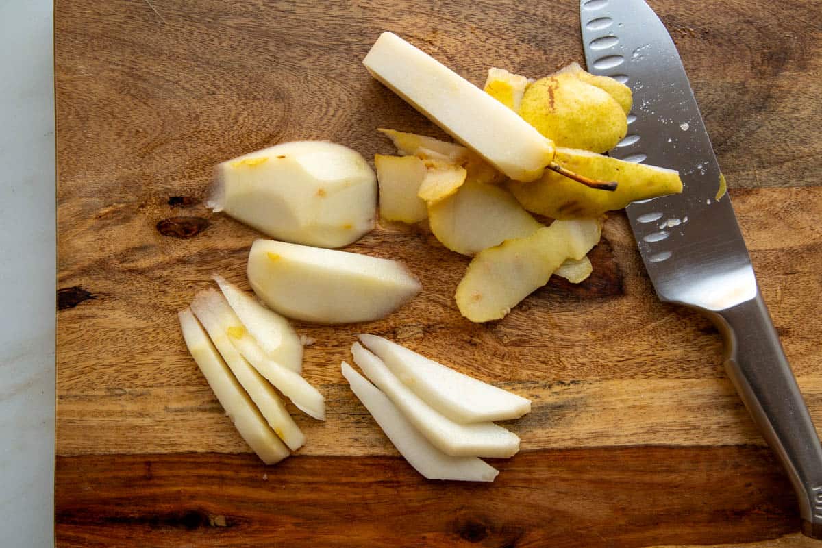 Sliced pears on a wooden cutting board next to a large silver knife.