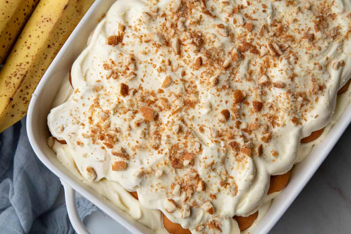 the top of a no cook banana pudding in a white baking dish next to bananas.