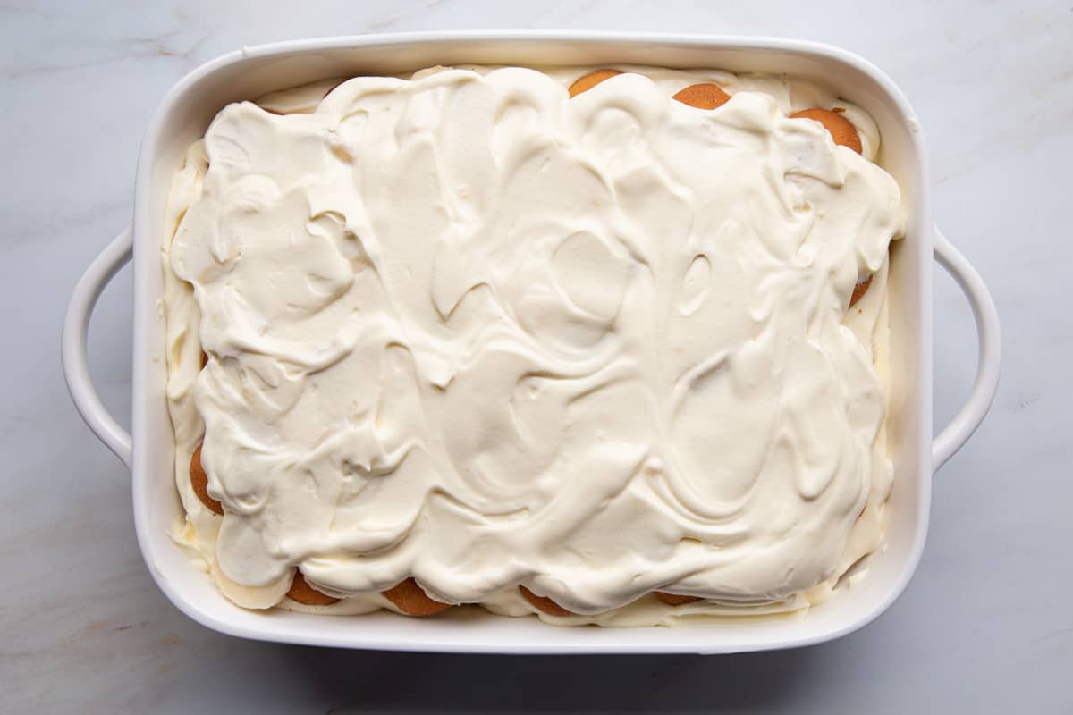 whipped topping spread all over the top of no cook banana pudding in a white baking dish.
