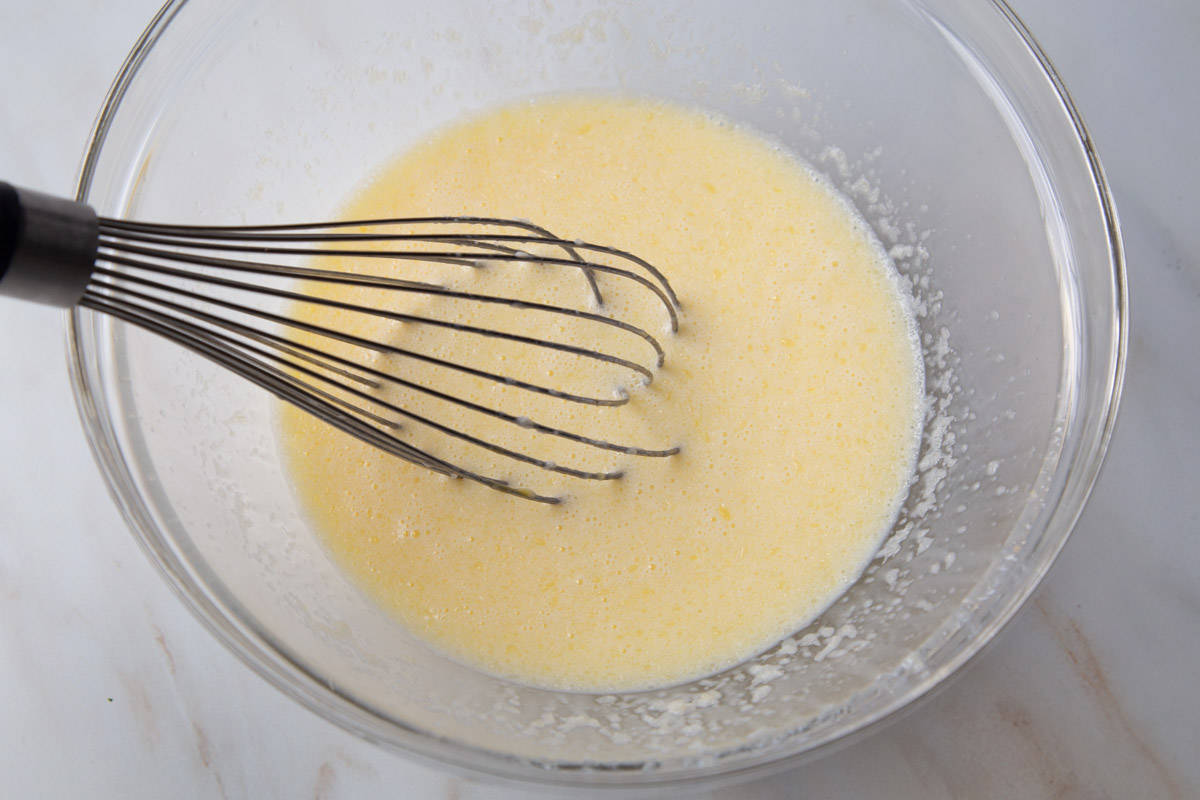 eggs, milk, and butter whisked together in a glass mixing bowl.