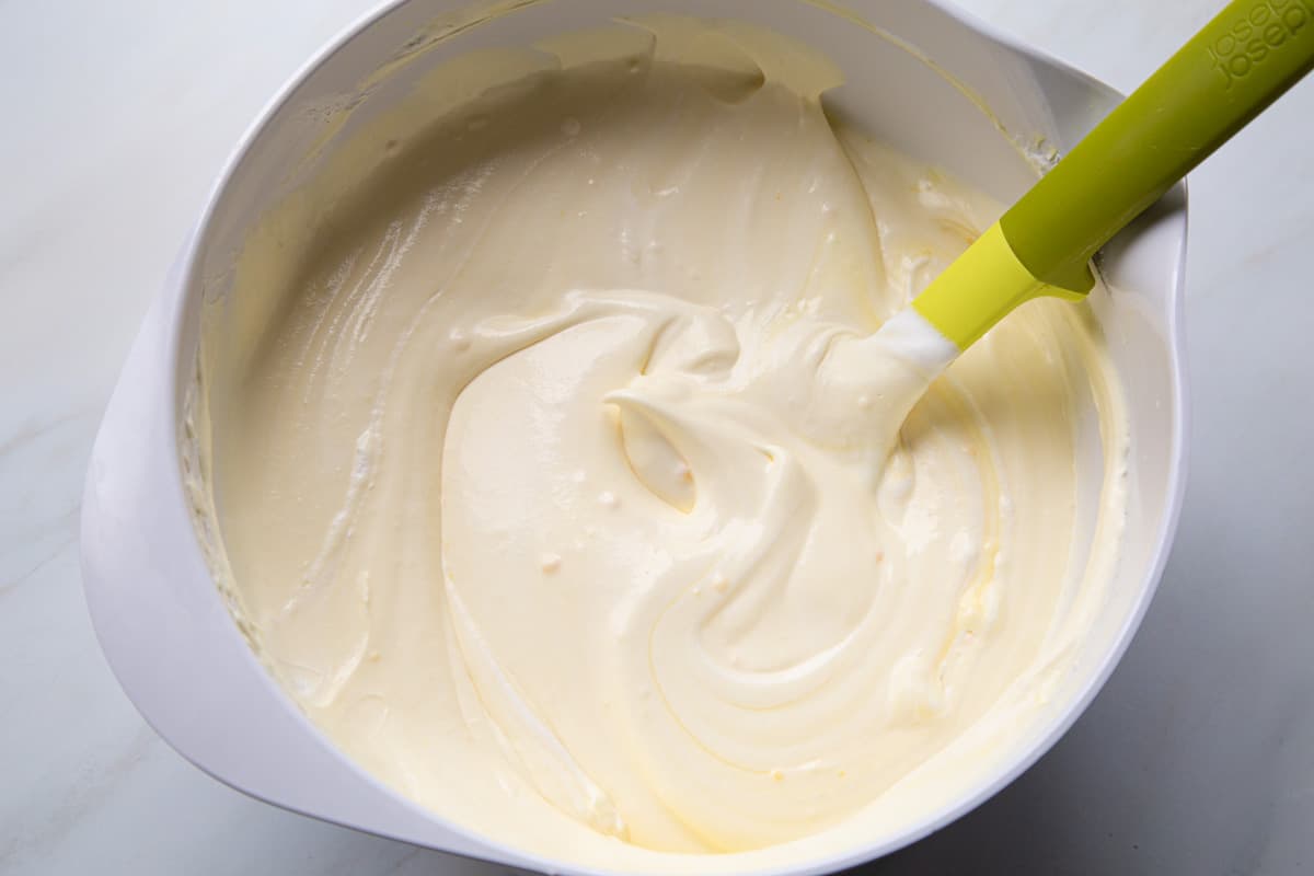 whipped topping mixture in a white mixing bowl with a green spatula.