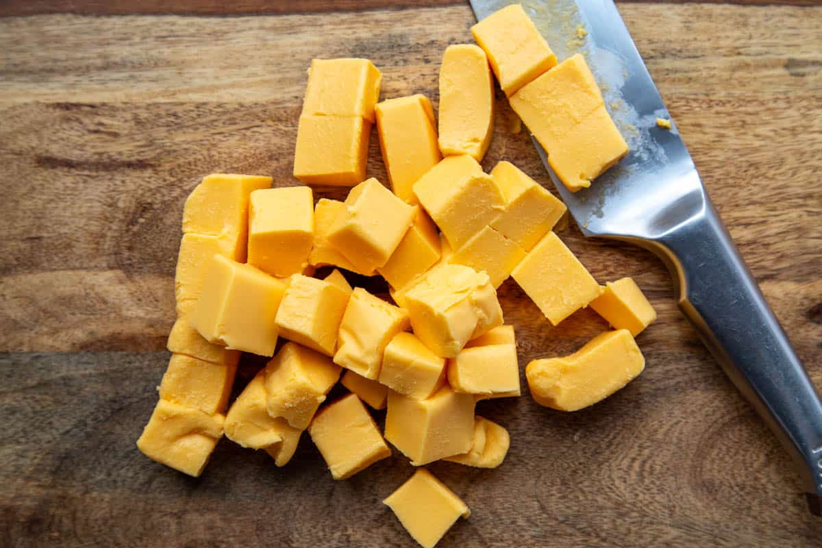 cubed velveeta on a wooden cutting board next to a knife.