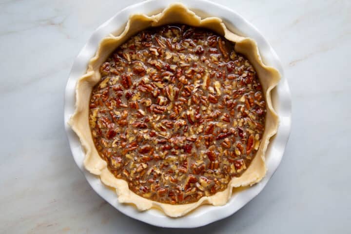 unbaked pie shell with a pecan filling in a white pie dish.