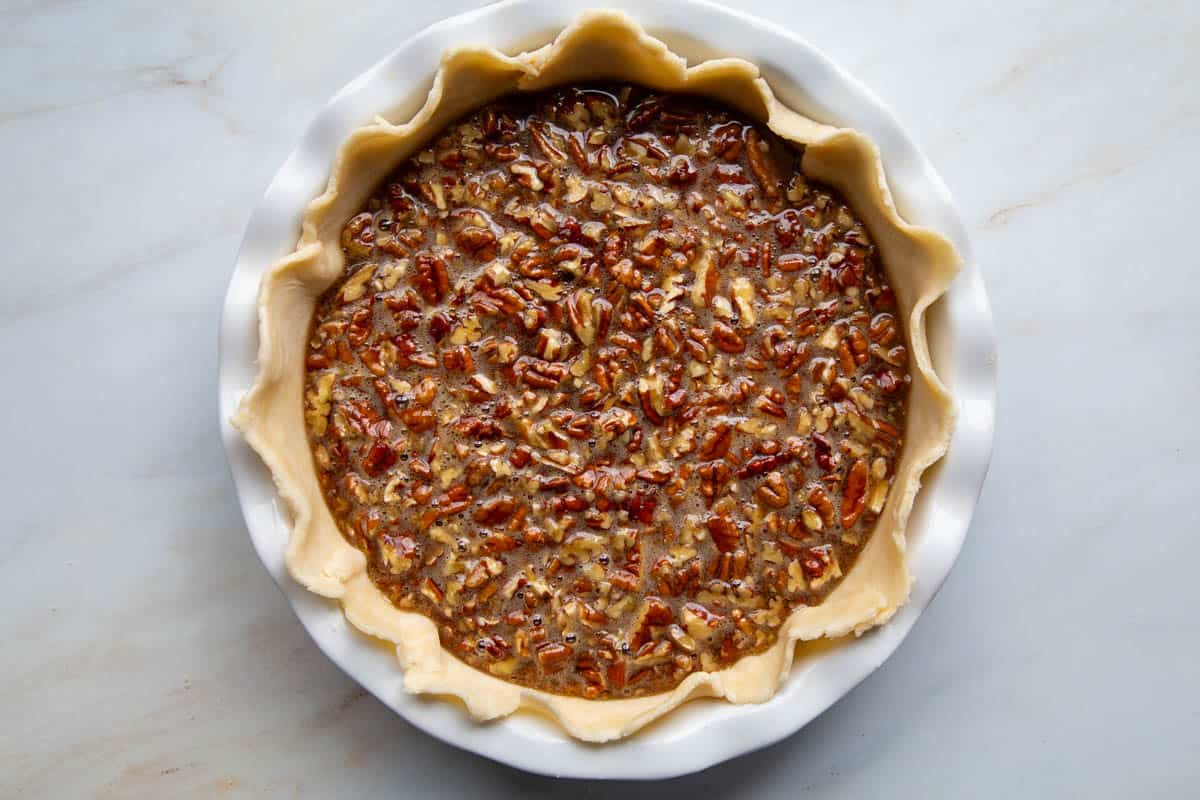 unbaked pie shell with a pecan filling in a white pie dish.