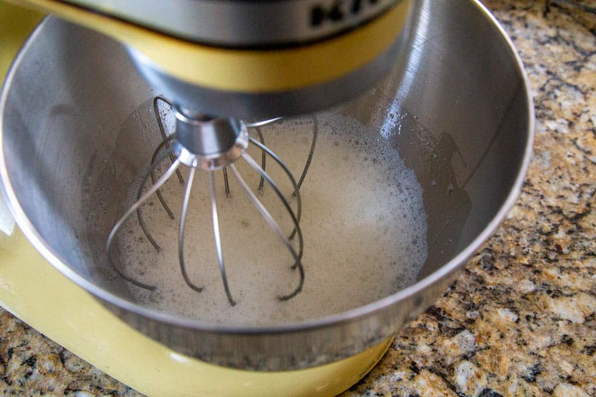 foamy egg whites in a yellow stand mixer.