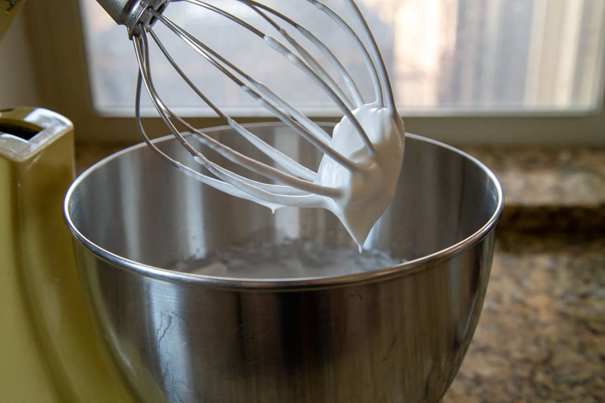 whipped meringue on a whisk attachment over a mixing bowl.