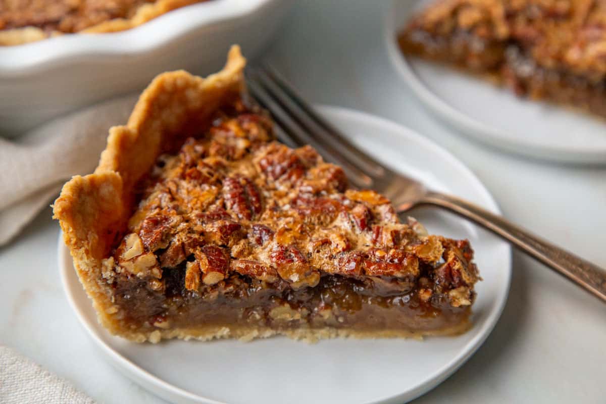 slice of old fashioned pecan pie on a white plate with a fork.