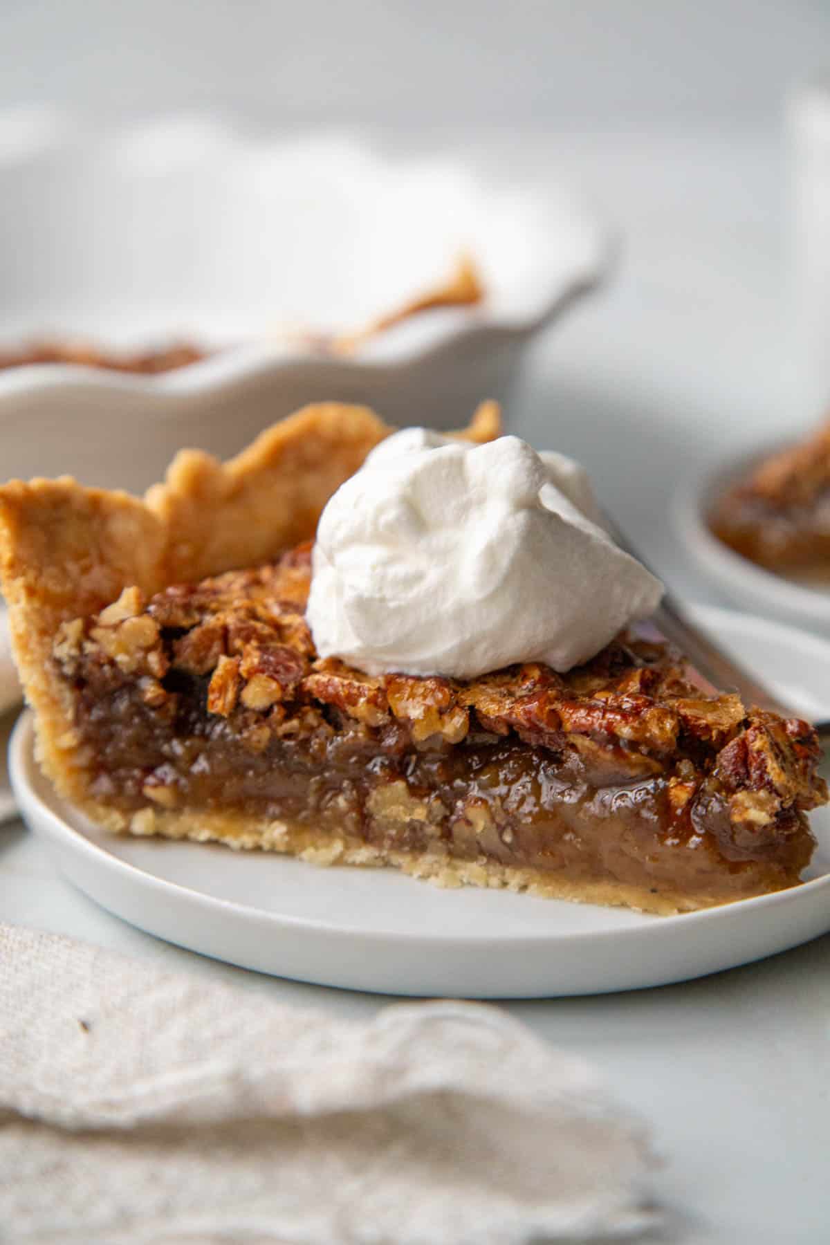 slice of pecan pie topped with whipped cream on a white plate.