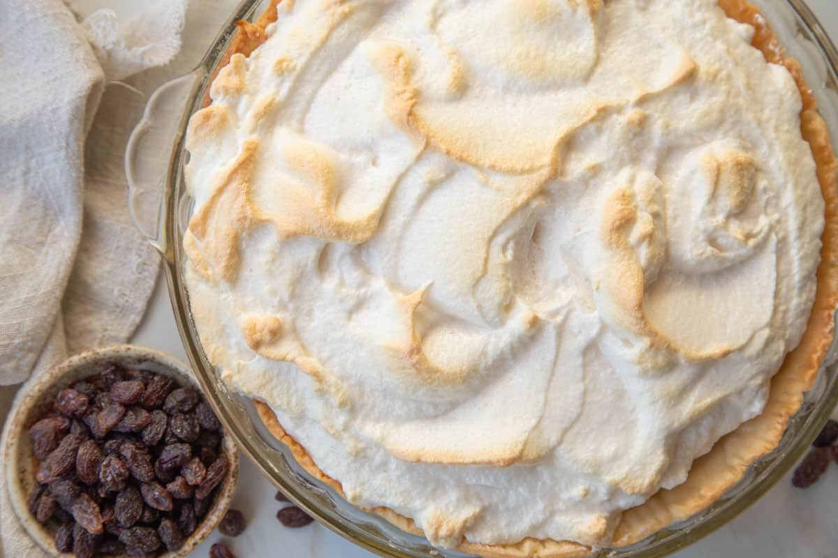 toasted meringue-topped sour cream raisin pie next to a small bowl of raisins.
