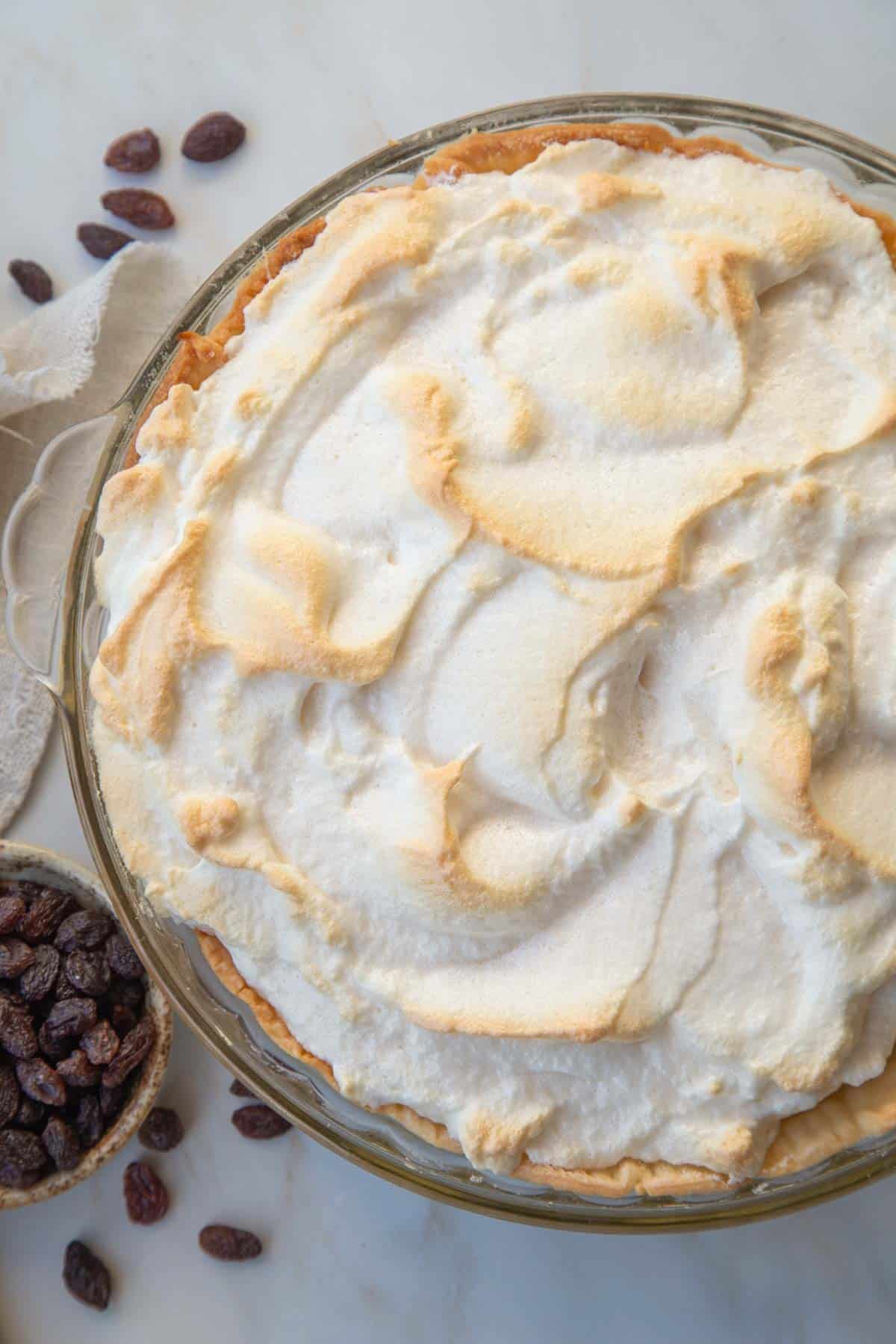 toasted meringue-topped sour cream raisin pie next to a small bowl of raisins.