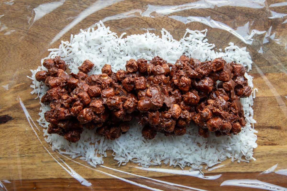 plastic wrap with a row of the chocolate marshmallow mixture on a row of shredded coconut.