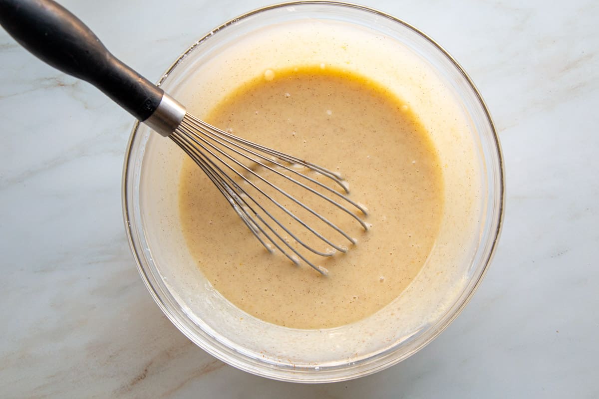 sour cream and egg mixture in a glass mixing bowl with a whisk.