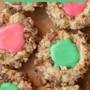 rows of round cookies with chopped pecans on the outside and a thumbprint indentation in the middle filled with pink and green icing.