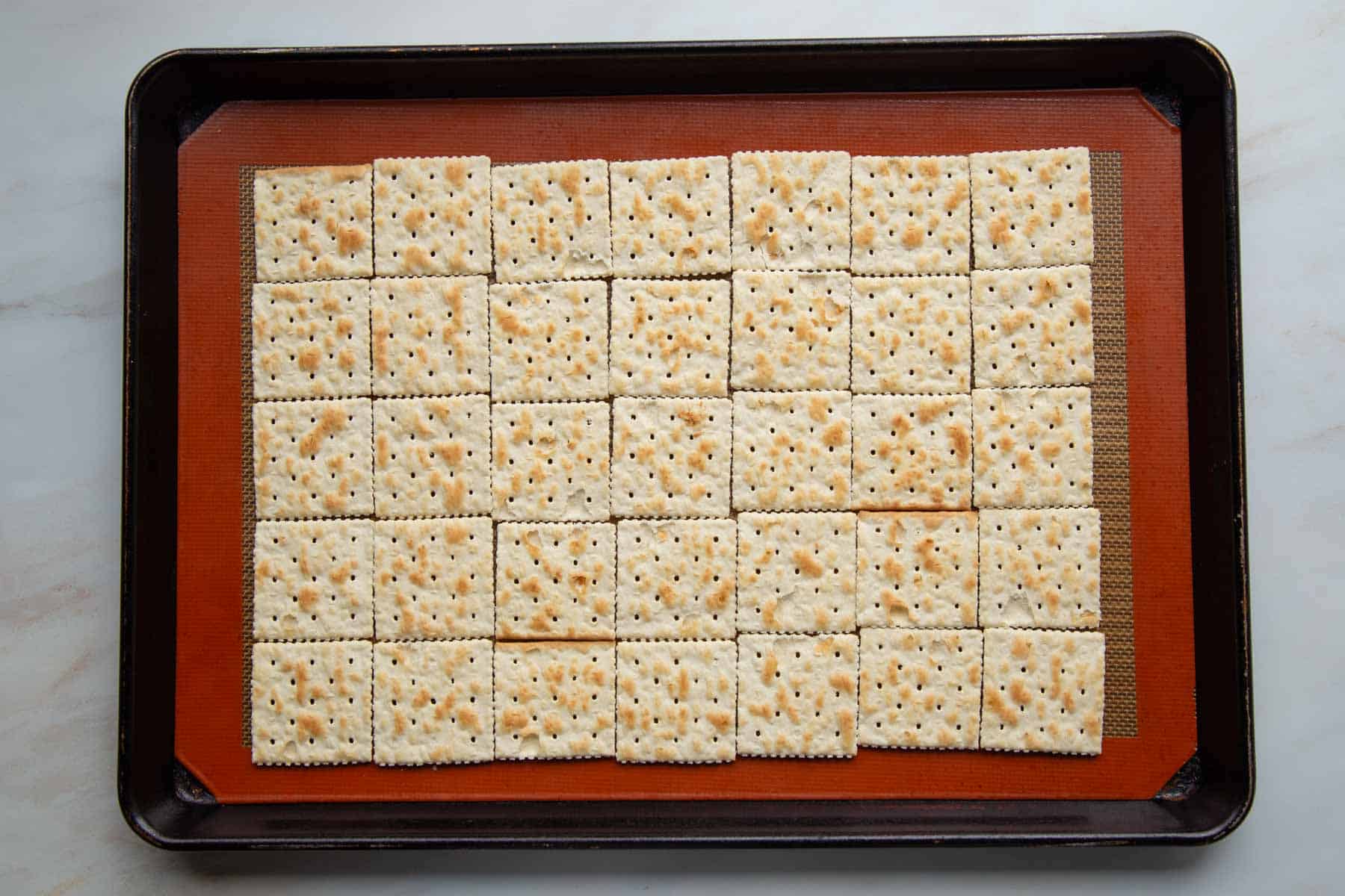 saltine crackers laid in rows on a silicone mat on a baking sheet.