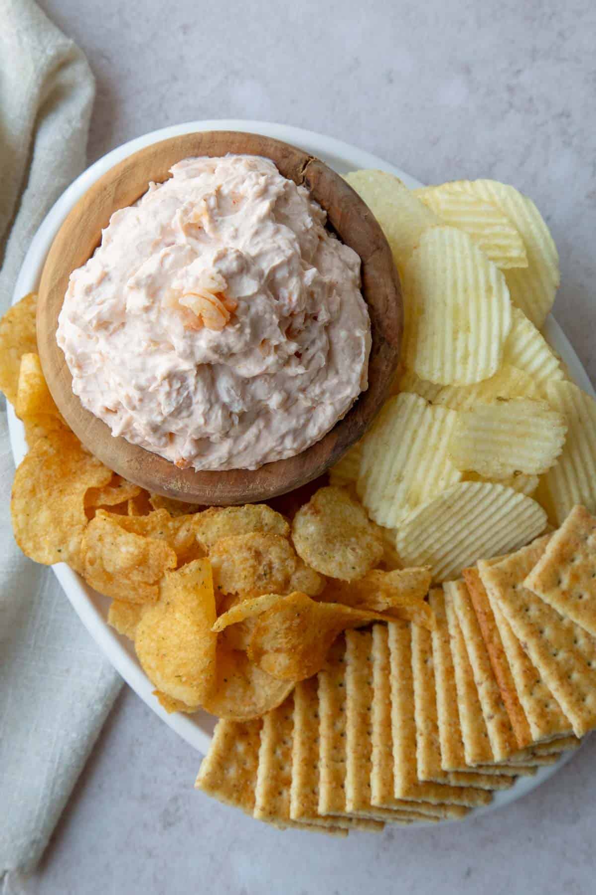 shrimp dip in a wooden bowl surrounded by chips and crackers.