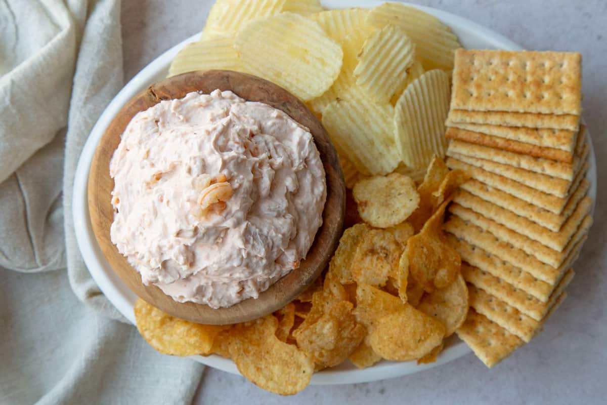 cream cheese shrimp dip in a wooden bowl on a platter with crackers and chips.