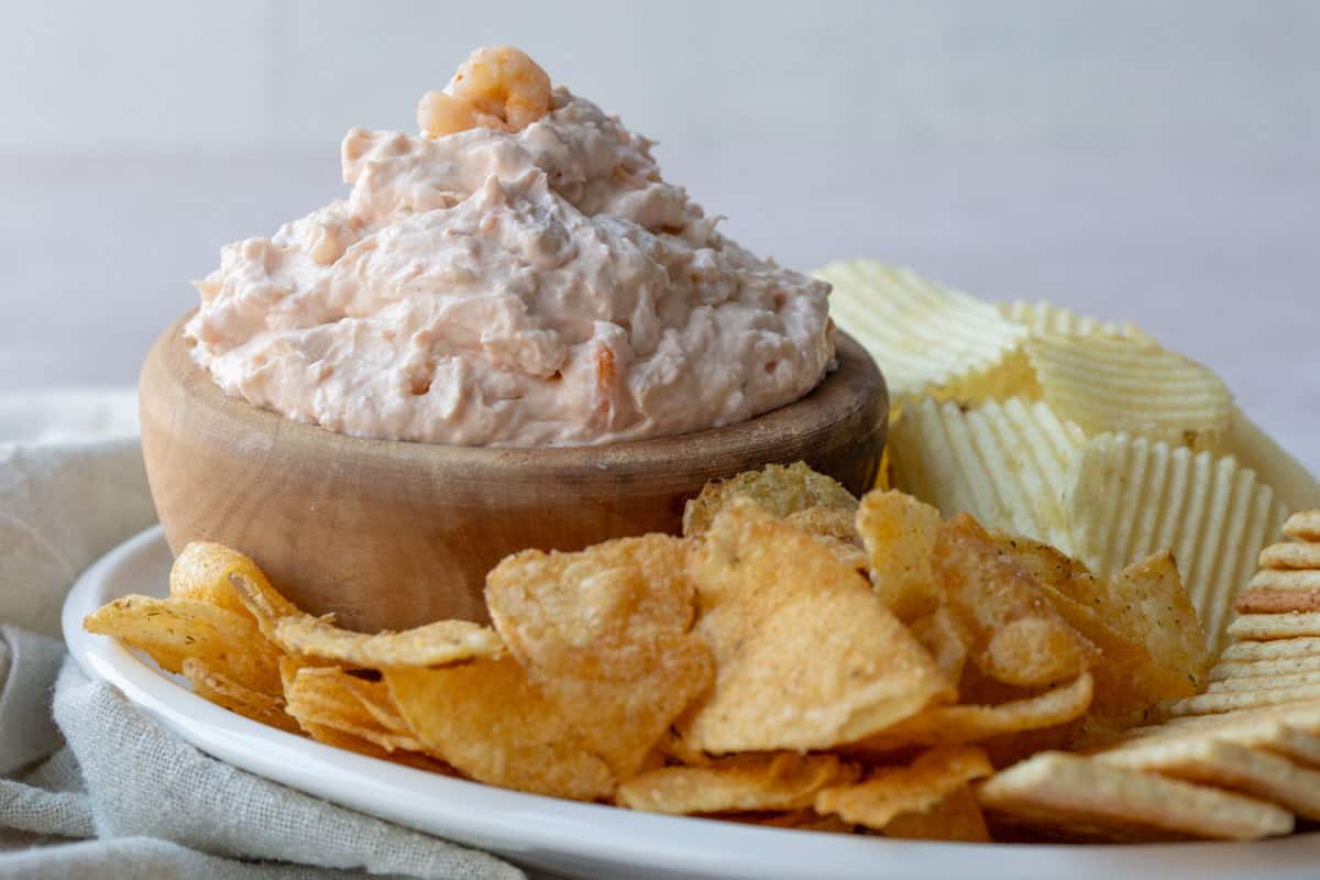 a bowl of shrimp dip next to chips and crackers.