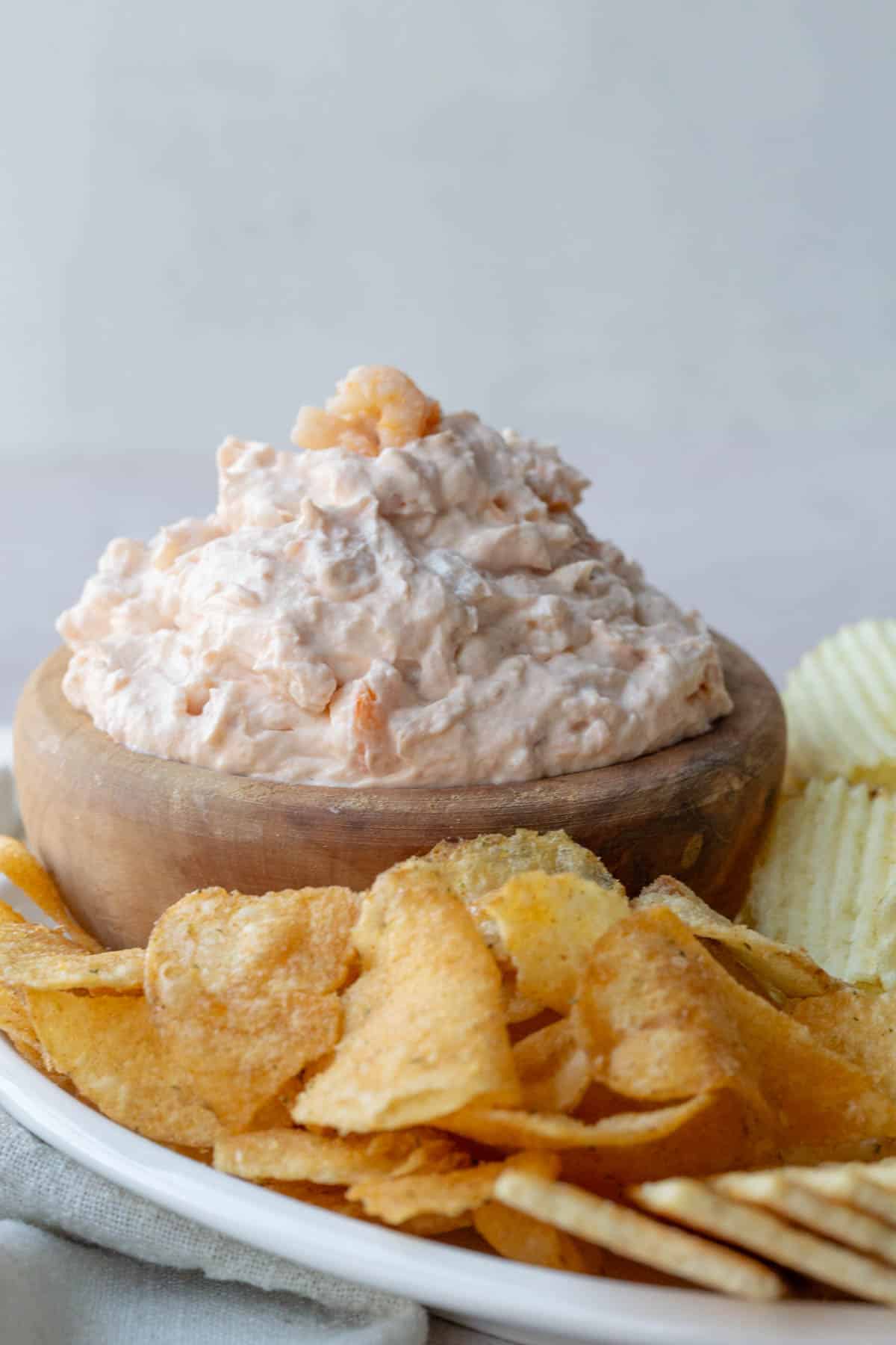 A wooden bowl filled with shrimp dip next to chips and crackers.