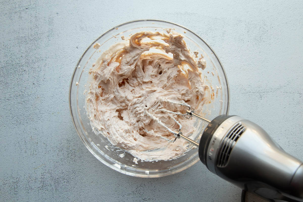 hand mixer blending ingredients for dip in a mixer bowl.